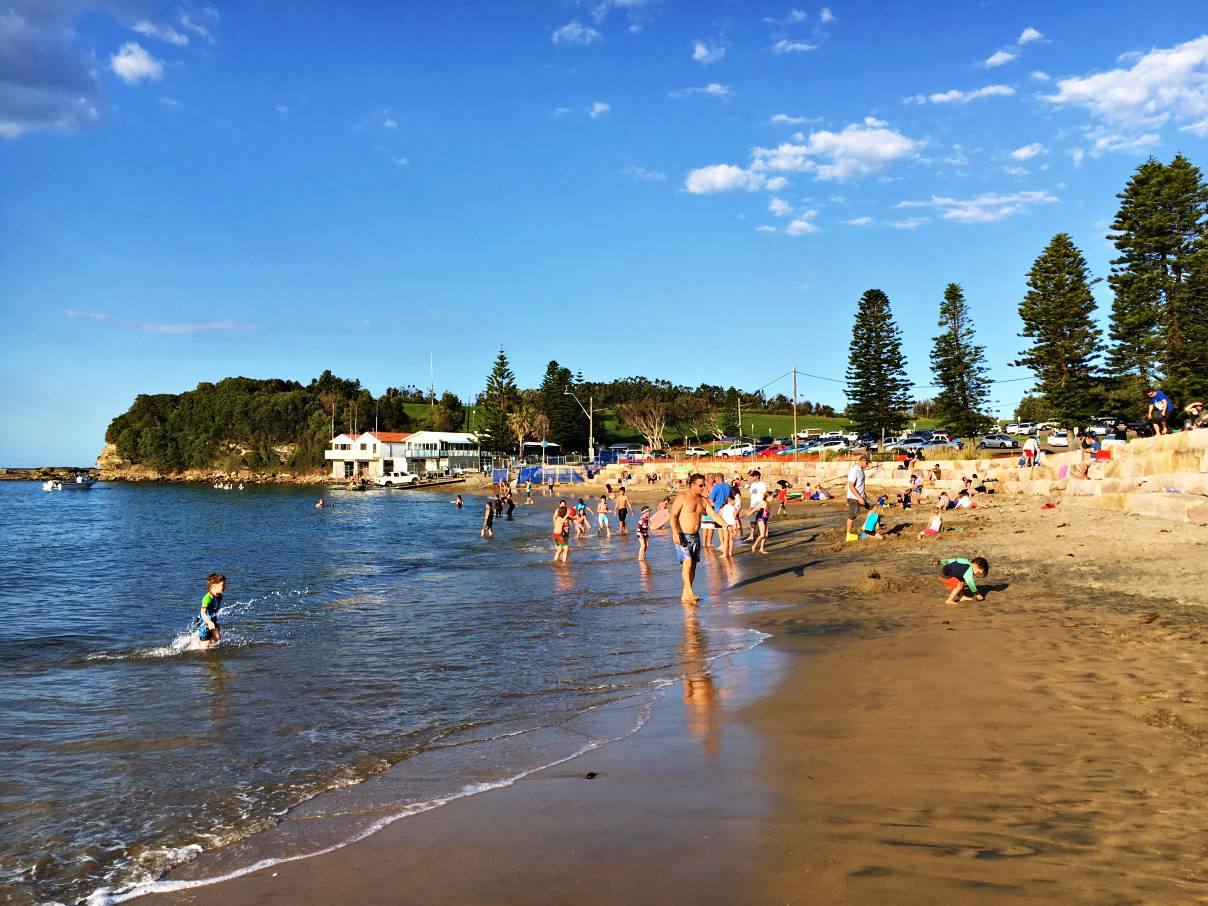 The Haven, Terrigal. A young boy runs through the water in the foreground while other children and parents play in the sand and water in the background.