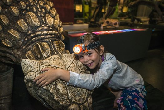 Girl with head-torch hugging a dinosaur